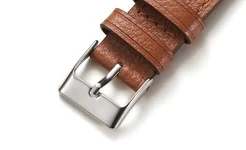 Close-up of a silver-finish pin buckle on a textured brown leather band, highlighting its classic rectangular frame and adjustable tongue.