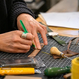 Detailed close-up of an artisan’s hands executing precision edge-folding (rembordé), highlighting the human expertise and technical mastery required for high-end bespoke manufacturing.